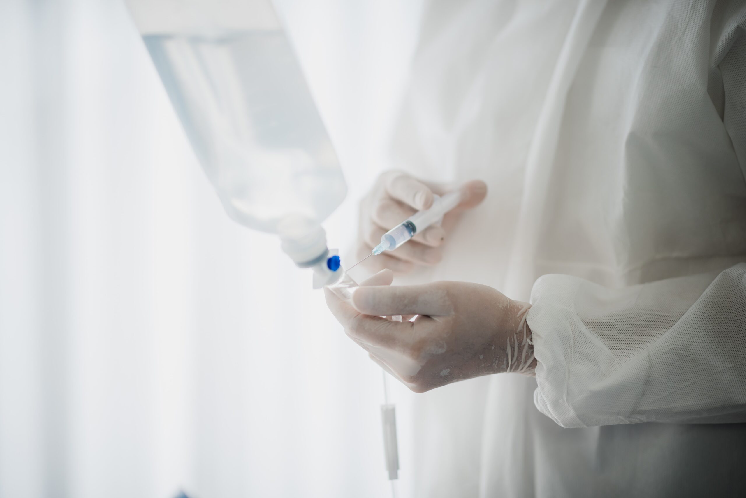 needle pressing into IV bag, white background and white person