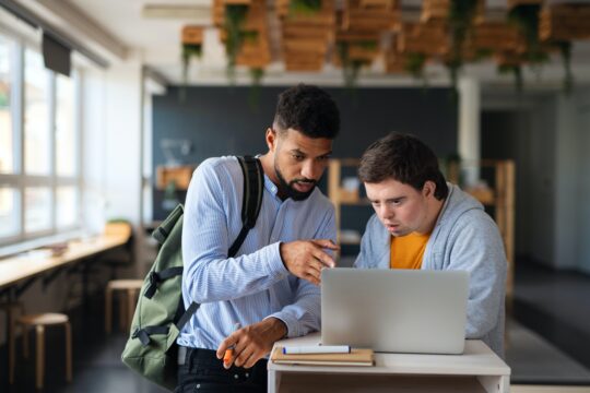 two men look at computer while one points to screen