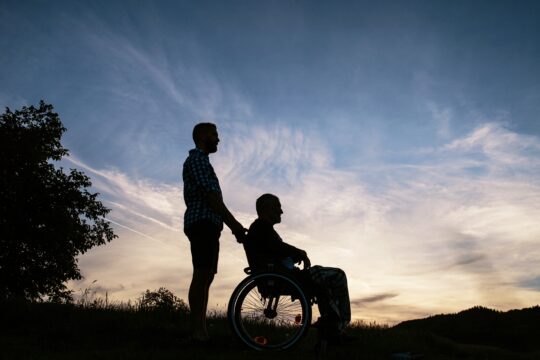 Silhouettes of man and man in wheelchair
