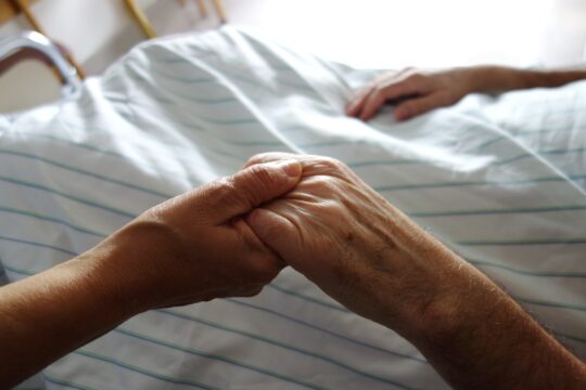 hands held together across a hospital bed